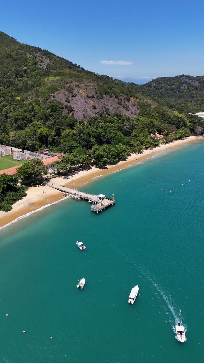 Vista vertical da Ilha Anchieta com o mar verde e barcos chegando ao píer